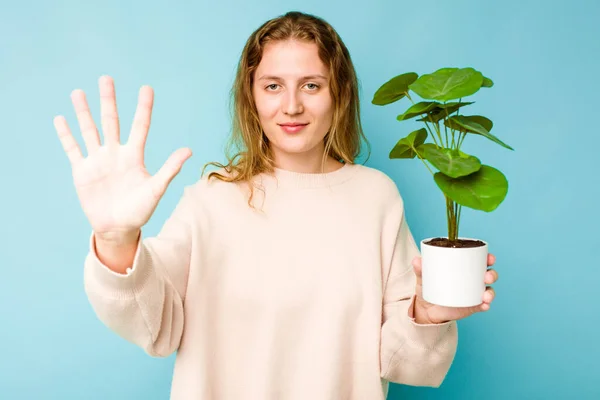 Fiatal Kaukázusi Kezében Egy Növény Elszigetelt Kék Háttér Mosolygós Vidám — Stock Fotó