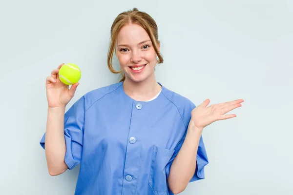 Young Caucasian Physiotherapist Holding Tennis Ball Isolated Blue Background Showing — Stock Photo, Image