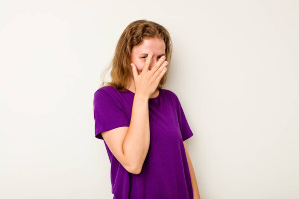 Young caucasian woman isolated on white background blink at the camera through fingers, embarrassed covering face.