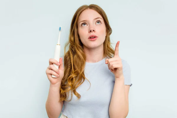 若いですCaucasian女性を持っています電動歯ブラシ隔離上の青の背景を指します逆さまにオープン口 — ストック写真