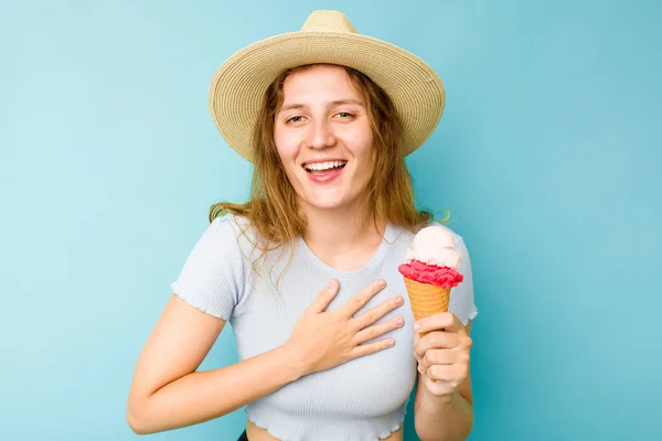 年轻的高加索女人拿着冰淇淋 隔离着蓝色的背景 大声笑着把手放在胸前 — 图库照片