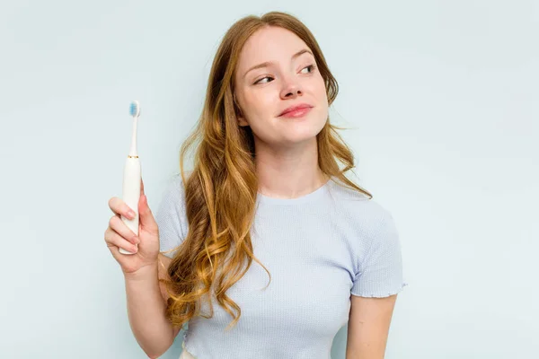 青い背景に孤立した電動歯ブラシを持つ若い白人女性目標と目的を達成することを夢見て — ストック写真