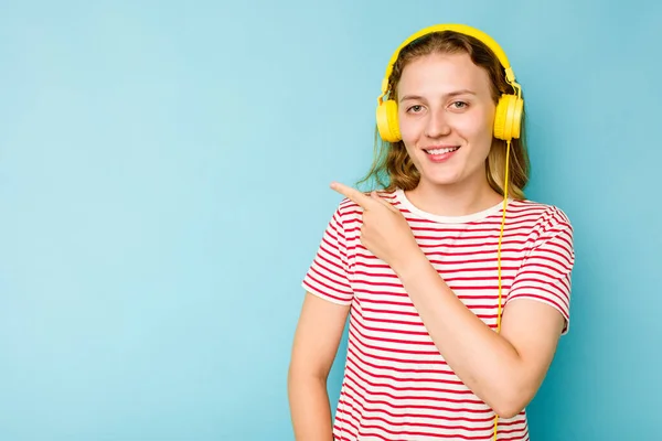 Mladá Běloška Nosí Sluchátka Izolovaná Modrém Pozadí Usmívá Ukazuje Něco — Stock fotografie