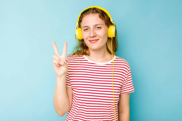Mladá Běloška Nosí Sluchátka Izolované Modrém Pozadí Ukazující Číslo Dvě — Stock fotografie