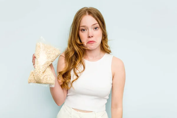 Young Caucasian Woman Holding Oatmeal Isolated Blue Background Shrugs Shoulders — Stock Photo, Image