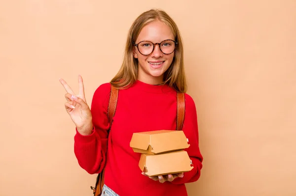 小高加索女学生拿着因米色背景而被隔离的汉堡包 快乐而无忧无虑 用手指展示一个和平的象征 — 图库照片