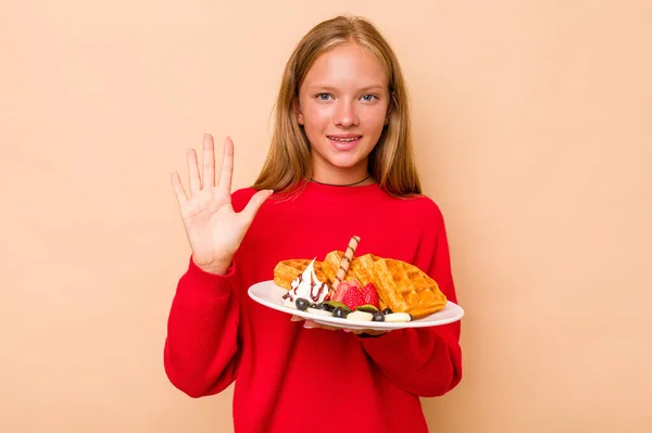 卡卡西亚小女孩拿着一个因米色背景而被隔离的华夫饼 开心地微笑着 带着五号手指 — 图库照片