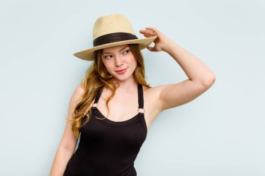 Kafkasyalı genç bir kadın kumsala gidiyor. Mavi arka planda izole bir şekilde. Kafasının arkasına dokunuyor, düşünüyor ve bir seçim yapıyor..