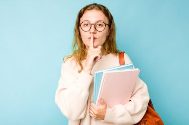 Mavi arka planda izole edilmiş genç beyaz kadın bir sır saklıyor ya da sessizlik istiyor..