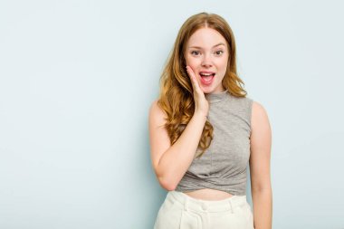 Mavi arka planda izole edilmiş genç beyaz kadın yüksek sesle bağırıyor, gözlerini açık ve ellerini gergin tutuyor..