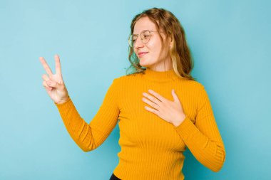 Beyaz bir kadın mavi arka planda izole edilmiş yemin ediyor, elini göğsüne koyuyor..