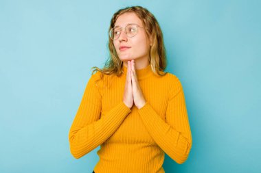 Kafkasyalı genç kadın mavi arka planda izole edilmiş dua ediyor, bağlılık gösteriyor, dindar biri ilahi ilham arıyor..