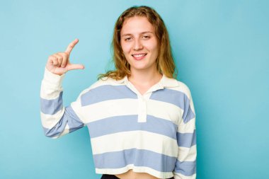 Kafkasyalı genç bir kadın mavi arka planda izole edilmiş. Elinde parmakları olan, gülümseyen ve kendinden emin bir şey var..