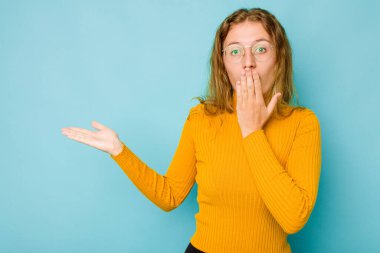 Mavi arka planda izole edilmiş genç beyaz kadın, avuç içinin fotokopi alanını tutmaktan etkilenmiş..