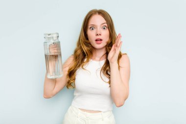 Kafkasyalı genç bir kadın elinde bir kavanoz su tutarken mavi arka planda izole edilmiş. Şaşırmış ve şok olmuş..