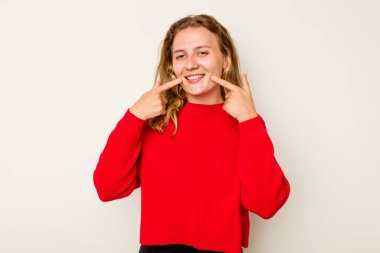 Beyaz arka planda izole edilmiş genç beyaz kadın gülümsüyor, parmaklarını ağıza doğrultuyor..