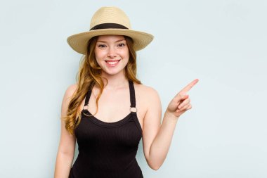 Mavi arka planda izole bir şekilde kumsala giden beyaz bir kadın gülümsüyor ve boş alanda bir şeyler gösteriyor..