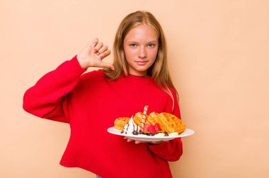 Kafkasyalı küçük bir kız bej arka planda izole edilmiş waffle tutuyor gururlu ve kendinden emin hissediyor, örnek olarak.