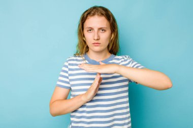 Mavi arka planda izole edilmiş genç beyaz kadın bir mola hareketi gösteriyor..