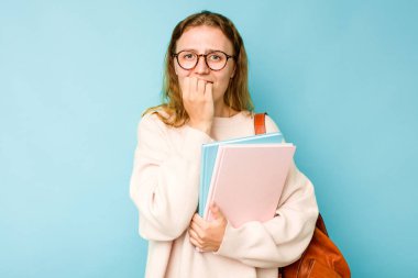 Mavi arka planda izole edilmiş, tırnak yiyen, gergin ve endişeli genç bir beyaz kadın..