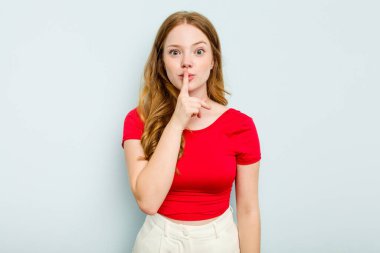 Mavi arka planda izole edilmiş genç beyaz kadın ya sır saklıyor ya da sessizlik istiyor..