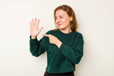 Beyaz arka planda izole edilmiş genç beyaz kadın gülümseyerek beş numarayı parmaklarıyla gösteriyor..