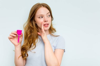 Mavi arka planda aybaşı fincanı tutan genç beyaz kadın gizli sıcak fren haberini veriyor ve yana bakıyor.