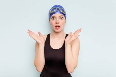 Genç beyaz yüzücü kadın mavi arka planda izole edilmiş şaşırmış ve şok olmuş..