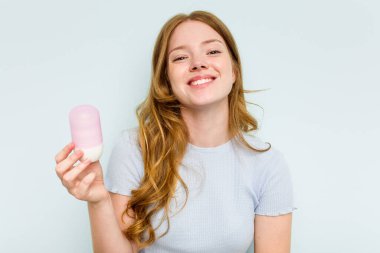 Mavi arka planda deodorant tutan genç beyaz kadın gülüyor ve eğleniyor..