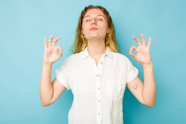 Mavi arka planda izole edilmiş genç beyaz kadın yoğun bir günün ardından rahatlıyor, yoga yapıyor..