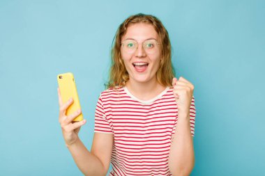 Mavi arka planda cep telefonu tutan beyaz bir kadın var.