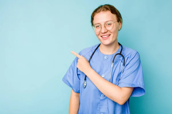 青い背景色の中に隔離された若い看護師の白人女性は笑って指摘し 何もない空間で何かを示す — ストック写真