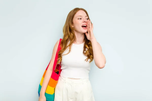 stock image Young caucasian woman holding LGTBI bag isolated on blue background shouting and holding palm near opened mouth.