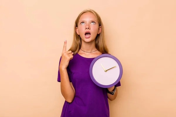 Little Caucasian Girl Holding Clock Isolated Beige Background Pointing Upside — Stock Photo, Image