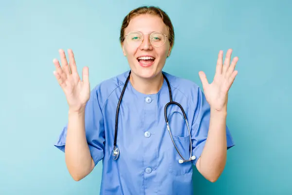 年轻的护士高加索女人 被隔离在蓝色的背景下 得到了一个愉快的惊喜 兴奋地举起双手 — 图库照片