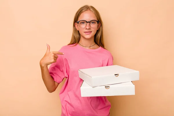 一个拿着比萨饼的高加索小女孩 被米色背景的人隔离了 她用手指着衬衫的复制品空间 自豪而自信 — 图库照片