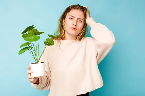 Młoda Biała Kobieta Trzymająca Roślinę Odizolowaną Niebieskim Tle Jest Szoku — Zdjęcie stockowe