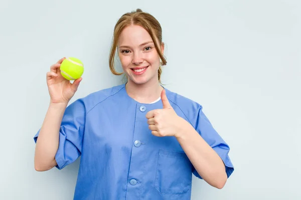 Ung Kaukasisk Sjukgymnast Håller Tennisboll Isolerad Blå Bakgrund Ler Och — Stockfoto