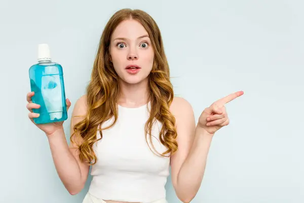 Young Caucasian Woman Holding Mouthwash Isolated Blue Background Pointing Side — Stock Photo, Image