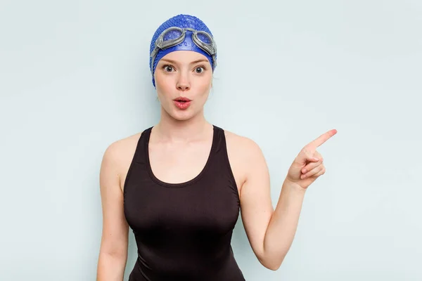年轻的高加索游泳女子 被蓝色背景隔离 指向侧边 — 图库照片