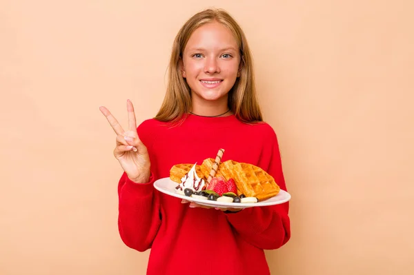 一个小高加索女孩手里拿着一个因米色背景而被隔离的华夫饼 手里拿着手指拿着二号 — 图库照片