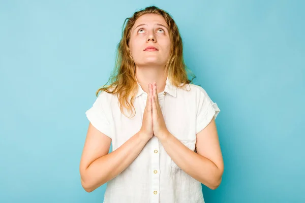 年轻的高加索女人被隔离在蓝色背景下 双手紧握着双手在嘴边祈祷 感到自信 — 图库照片