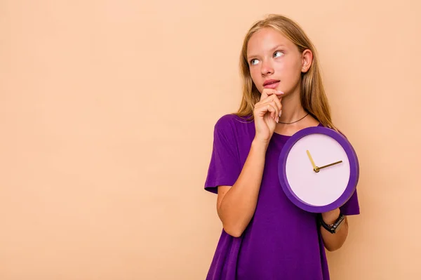 Menina Caucasiana Segurando Relógio Isolado Fundo Bege Olhando Para Lados — Fotografia de Stock