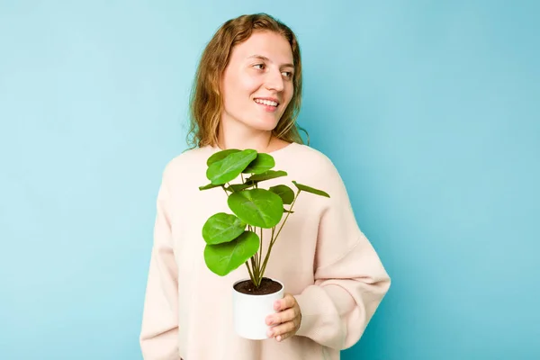 Young Caucasian Woman Holding Plant Isolated Blue Background Looks Aside — Stock Photo, Image