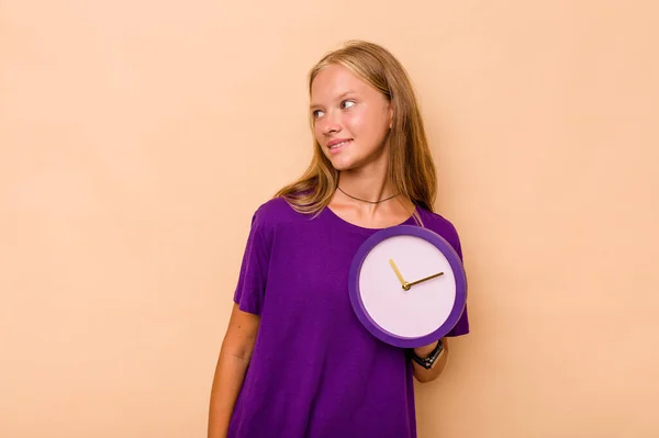 Menina Caucasiana Segurando Relógio Isolado Fundo Bege Olha Para Lado — Fotografia de Stock