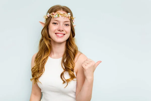 Young elf woman isolated on blue background points with thumb finger away, laughing and carefree.