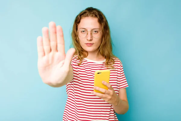 Mladá Běloška Drží Mobilní Telefon Izolovaný Modrém Pozadí Stojí Nataženou — Stock fotografie