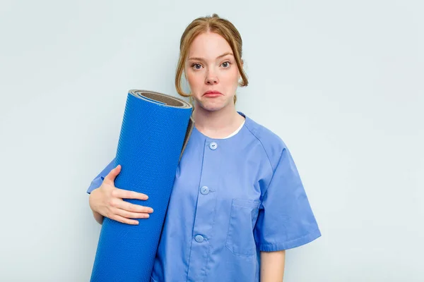 Young Caucasian Physiotherapist Holding Mat Isolated Blue Background Shrugs Shoulders — Stock Photo, Image