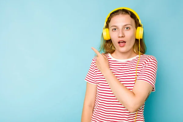 Młoda Biała Kobieta Nosi Słuchawki Odizolowane Niebieskim Tle Wskazując Bok — Zdjęcie stockowe