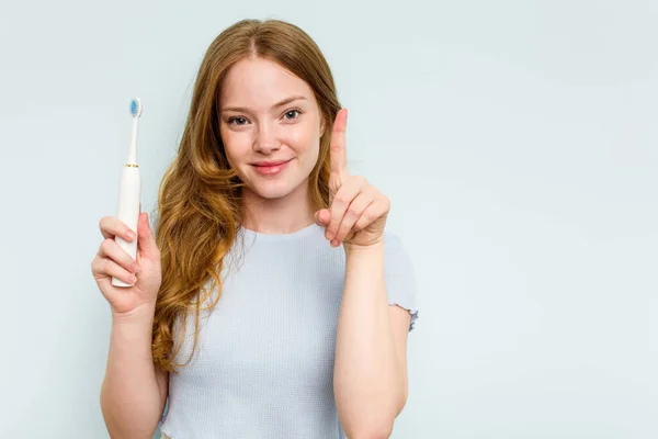 青地に電気歯ブラシを持つ若い白人女性は指でナンバーワンを示しています — ストック写真